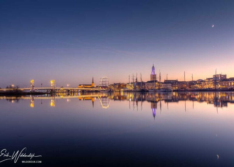 Foto van het verlichte stadsfront van Kampen spiegelend in het water van de IJssel