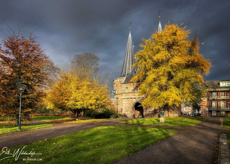 De Cellebroederspoort in Kampen in het zonlicht contratserend met een donkere buienlucht