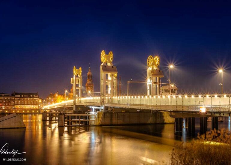 DE averlichte stadsbrug van Kampen en de Nieuwe Toren in het blauwe uur 's morgens met een beetje nevel