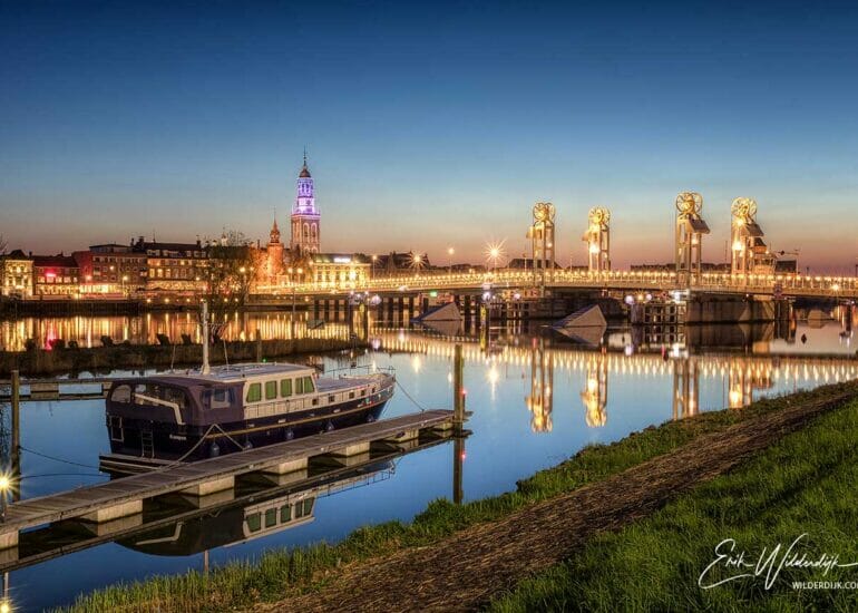 Het stadsfront van Kampen na zonsondergang, met gouden lichtval, gezien vanuit het Kikkergat met motorjacht op de voorgrond