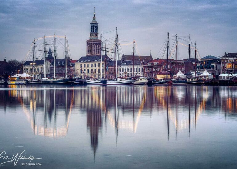 Schepen van de bruine vloot met lichtjes in de masten voor het stadsfront van Kampen aan het begin van de dag