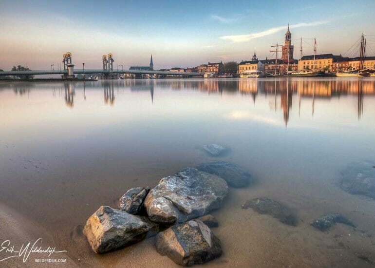 Stadsfront Kampen in het eerste zonlicht na zonsopkomst met stenen in het water op de voorgrond