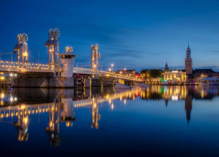 Avondfoto van het IJsselfront van Kampen met brandende verlichting en weerspiegeling in het wateroppervlak van de IJssel